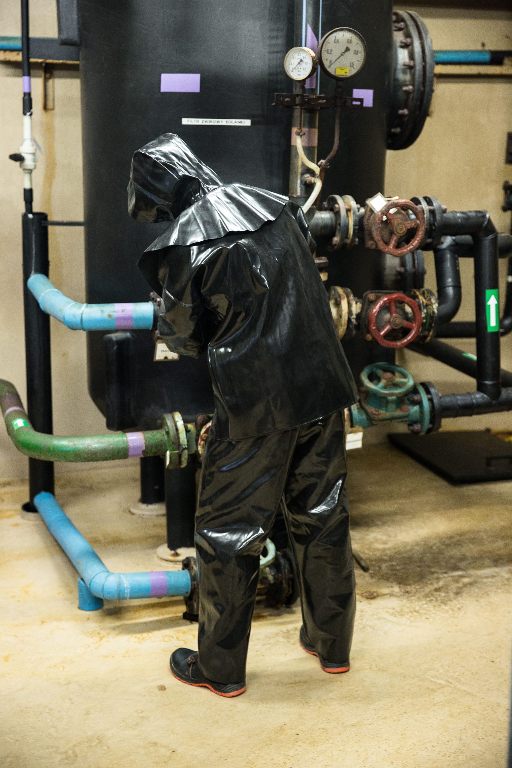 Worker in black protective suit managing industrial equipment indoors.